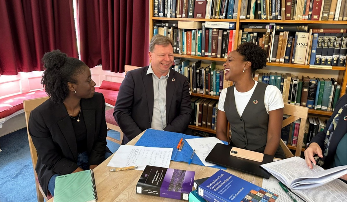 Two female students and mentor sitting around the table. A bookcase in the background