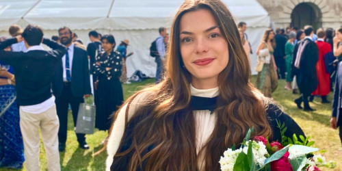 Alexandra posing for photo at the graduation ceremony holdinga a flower bouquet