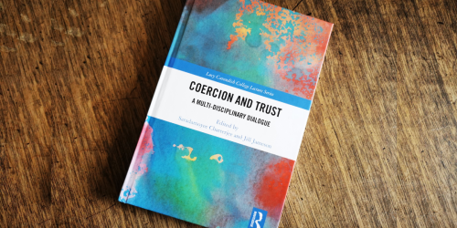 Coercion and Trust book (colourful cover) on wooden table