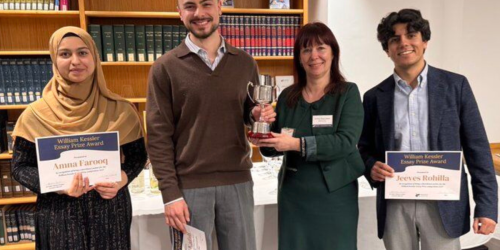 A photograph of four people standing in front of a bookshelf filled with legal or academic books in a formal setting. 