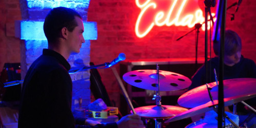 Wynn Tasker playing drums in neon-lit room