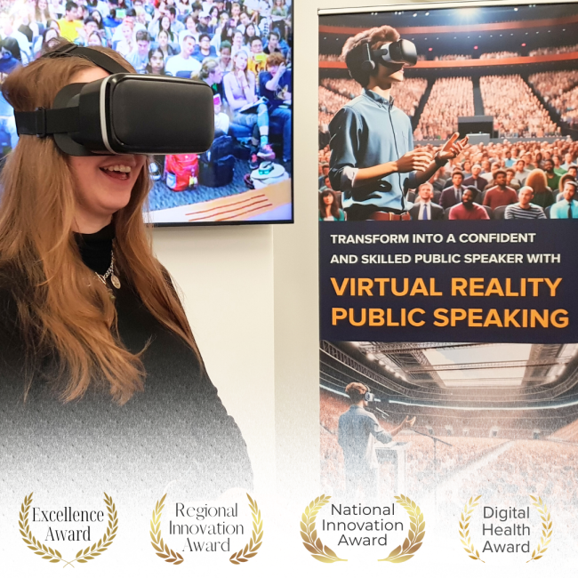 A woman wearing a virtual reality headset smiles while immersed in a VR experience. Behind her is a large screen showing an image of a crowded auditorium, and next to her is a banner promoting "Virtual Reality Public Speaking." The banner features an illustration of a person wearing a VR headset, practicing public speaking in front of a large virtual audience, with the tagline: "Transform into a confident and skilled public speaker with Virtual Reality Public Speaking.